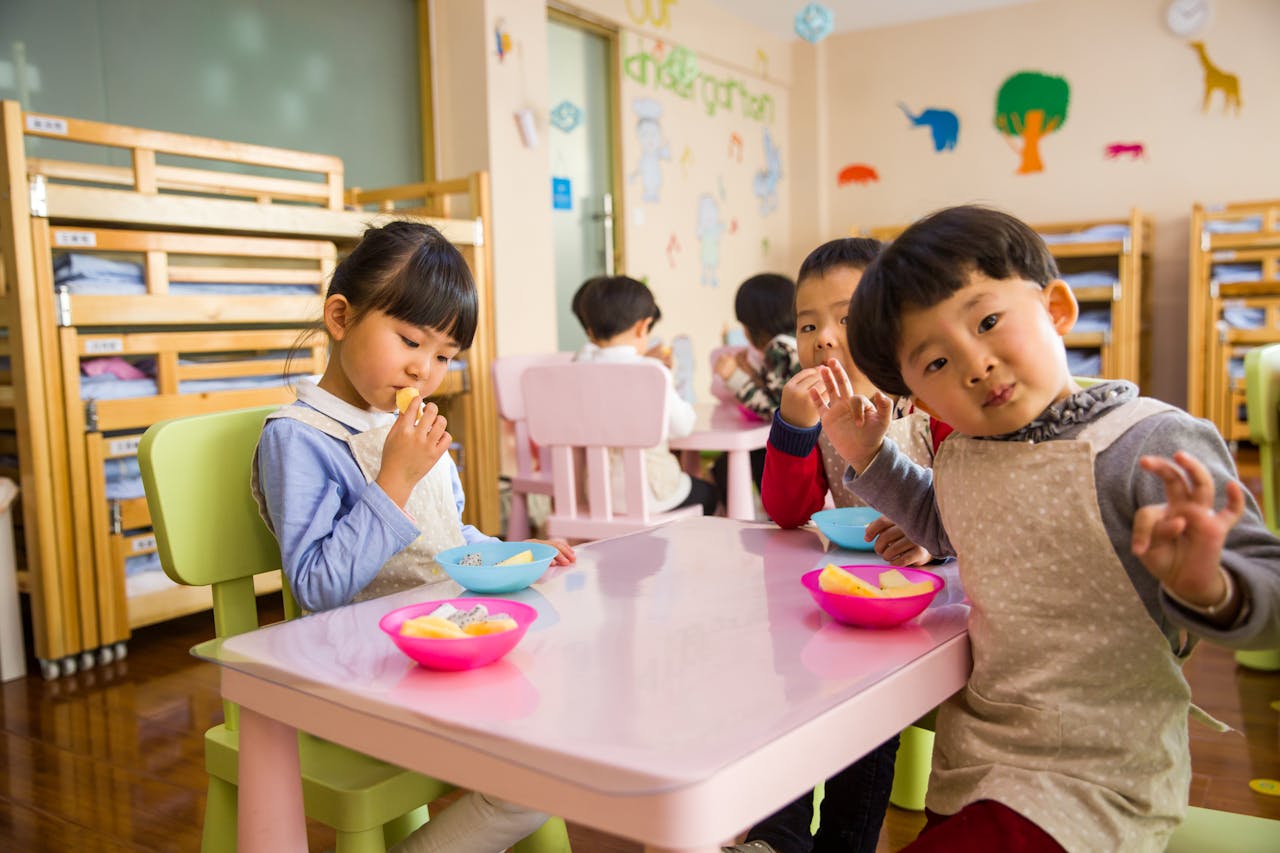 our-journey-01 Kids seated around a table in a colorful classroom, eating snacks happily.