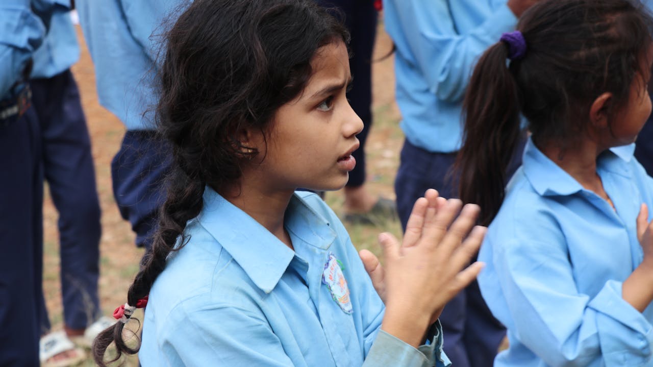 services-03 Children in uniforms clapping during an outdoor school activity.